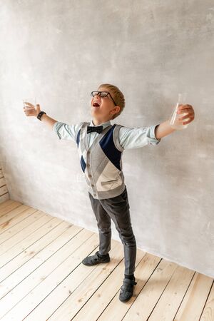 Young boy wearing black trousers and white sweater posing with two flasks in handsの写真素材