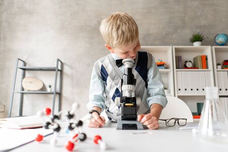 Little schoolboy in casual clothes looks in microscopeの写真素材