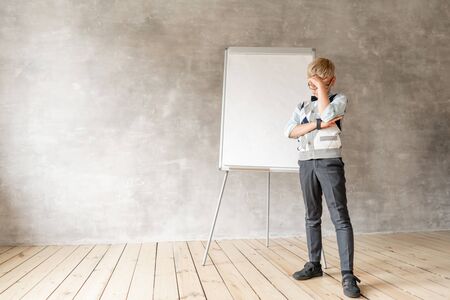 A little schoolboy in sweater and black trousers stands about with flip Board.の写真素材