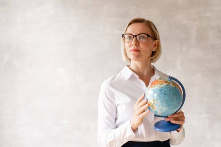 Charming teacher wearing blouse and skirt holds globe her handsの写真素材