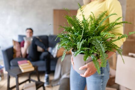 Woman in the foreground holding a fern flower in her hands. Young couple moving to a new apartment together. Relocation conceptの写真素材
