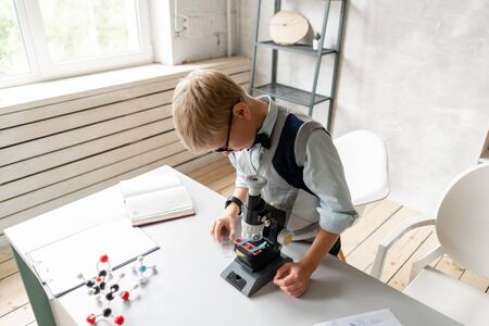 Schoolboy in glasses looks at sample on glass at chemistry lessonの写真素材