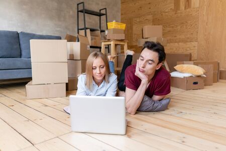 Happy Couple lying on floor together using computer wireless internet while moving into new home....