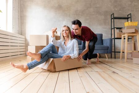 Happy couple having fun and riding in cardboard boxes at new home. Young couple moving to a new apartment together. Relocation conceptの写真素材