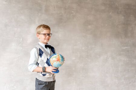 A blond schoolboy in glasses and a white sweater turns the globe and watches it spinの写真素材