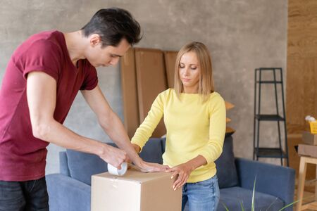 Close up of hand packing cardboard box, concept moving house. Young couple moving to a new apartment together. Relocation conceptの写真素材