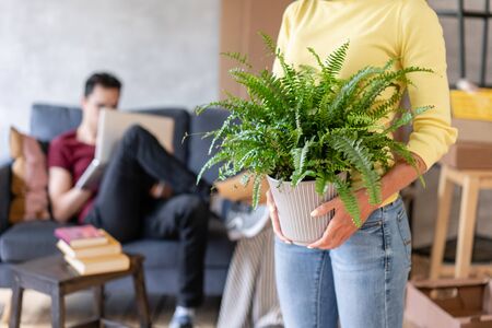 Woman in the foreground holding a fern flower in her hands. Young couple moving to a new apartment together. Relocation conceptの写真素材