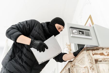The thief opens the electronic safe. The burglar commits a crime in Luxury apartment with stucco. Thief with black balaclava stealing safe box.の写真素材