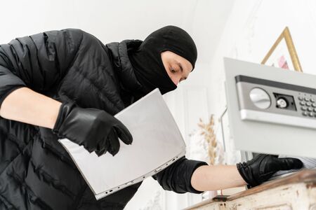 Thief with black balaclava stealing modern Electronic safe box. The burglar commits a crime in Luxury apartment with stucco.の写真素材
