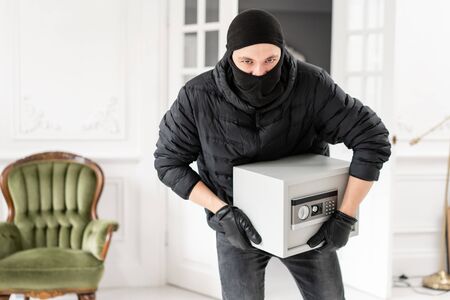 Thief looking at the camera with black balaclava stealing modern Electronic safe box. The burglar commits a crime in Luxury apartment with stucco.の写真素材
