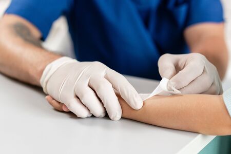 medical patch. Doctor in blue uniform make elastic bandaged around a boy hand with trauma in his arm. in the hospitalの写真素材