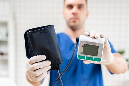 Male doctor in the hospital, holding blood pressure monitor, closeup. Medical object.の写真素材