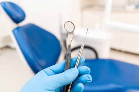 The hand of the dentist in the glove holds tool probe and mirror. . Stomatological instrument in the dentist clinic. Dental work in clinic. Office where dentist conducts inspection and concludes.の写真素材