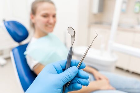 Close-up hand of dentist in the glove holds tool probe and mirror. The patient in the dental chair at the background. Dental work in clinic. Office where dentist conducts inspection and concludes.の写真素材