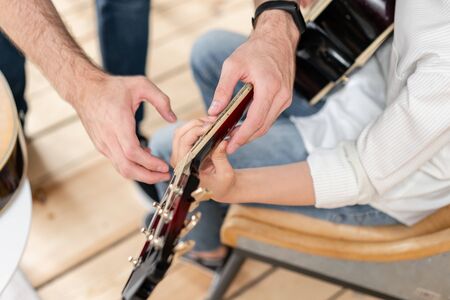 Closeup of acoustic guitar in hands of young boy in white shirt, who learn to play chords on guitarの写真素材