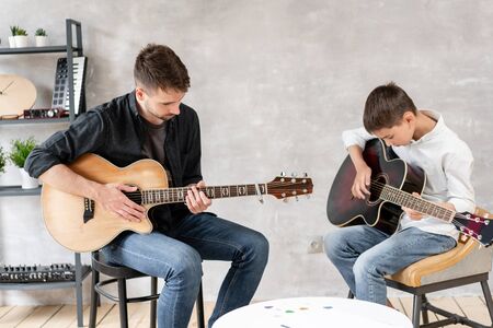 Confident teacher teaches his pupil to play basic chords. Musical education at homeの写真素材