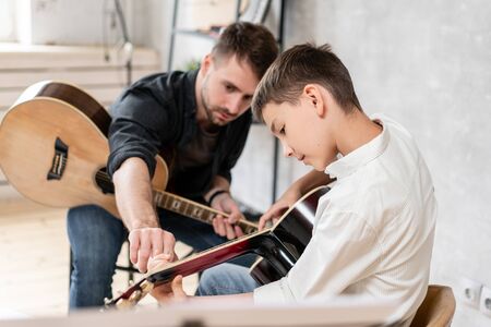 Adult man explains his son, who learn to play guitar, how to play studied chord correctly. Education with familyの写真素材