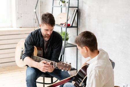The young teacher shows the correct position of the hands in the guitar on his exampleの写真素材