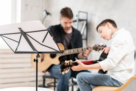 Young teenager and his older brother learining to play acoustic guitar togetherの写真素材