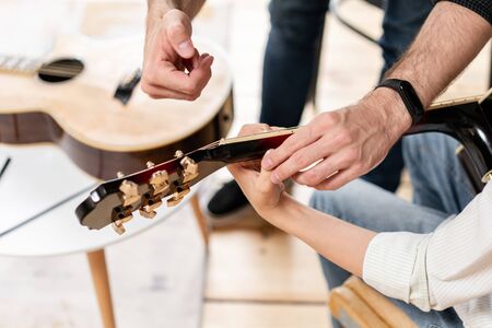 Closeup of guitar in hands of young boy with another guitar laying on the floor on the backgroundの写真素材