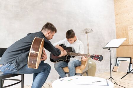 Two brother playing guitar. Older brother teaches younger one to play chords correctlyの写真素材