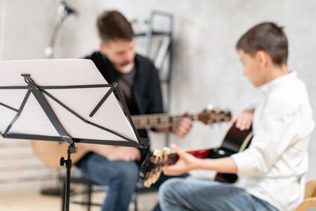 Closeup of music sheet with an adult man and young boy playing acoustic guitar on backgroundの写真素材