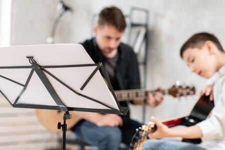 Music sheet standing in front of teacher and his young student playing guitarの写真素材