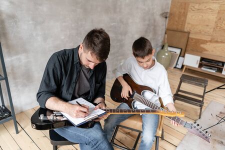 Adult man explains his son, who learn to play guitar, how to play melodies and songs using music sheet. Education with familyの写真素材