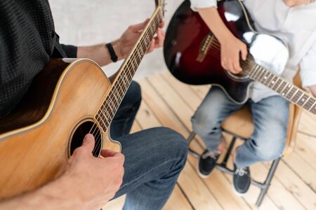 Two boys of different ages sitting with guitar in hands and playing itの写真素材