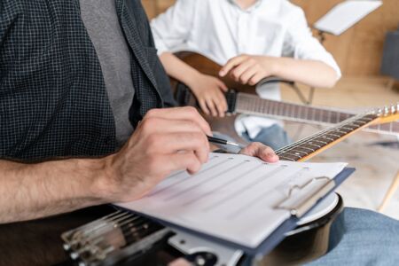Adult man explains his son, who learn to play guitar, how to play melodies and songs using music sheet. Education with familyの写真素材
