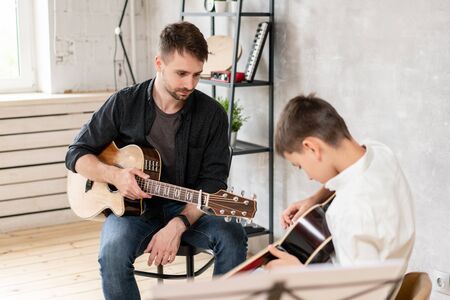 A professional teacher watches the movement of his students hands while he plays the guitarの写真素材