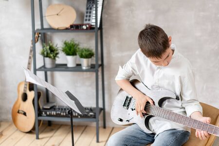 Teenager sits in chair behind sheet music and learning new melody for electric guitarの写真素材