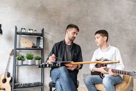 Two brothers of different ages talk to each other after guitar exerciseの写真素材
