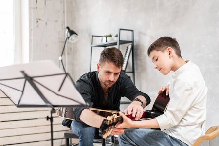 Adult man explains his son, who learn to play guitar, how to play studied chord correctly. Education with familyの写真素材