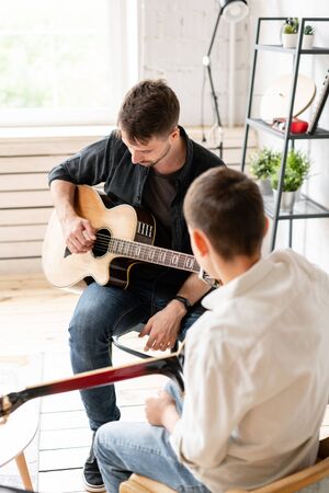The young teacher shows the correct position of the hands in the guitar on his exampleの写真素材