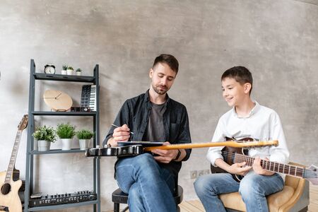 Little student watches at his music teacher who writes notes on music sheetの写真素材