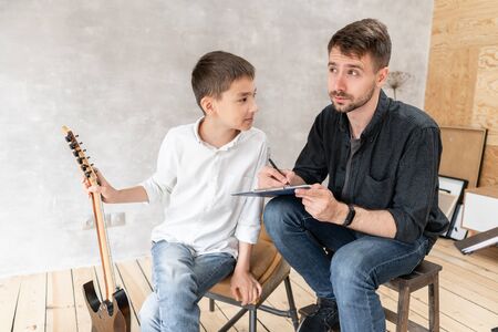 A personal tutor writes notes on music sheet for his student and explain how to play them.の写真素材