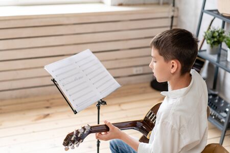 Teenager sits in chair behind sheet music and learning new melody for acoustic guitarの写真素材