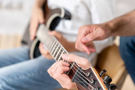 Adult man helps his little brother to learn how to play elecrtric guitarの写真素材