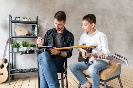 Two brothers of different ages sit in chairs with electric guitars in hands and posingの写真素材