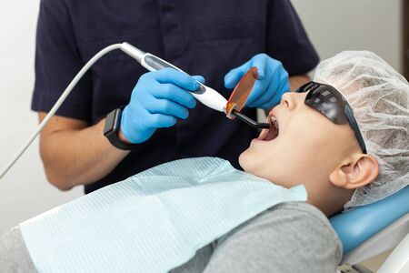 Young boy lays on dentist chair while his mouth examinated by UV lampの写真素材