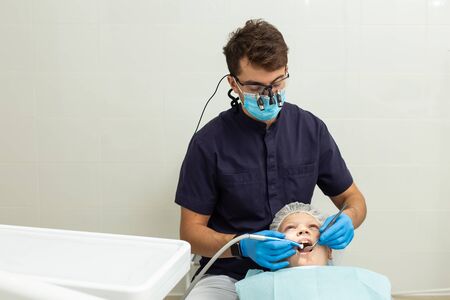 Dentist in black shirt drilling tooth of his young patientの写真素材