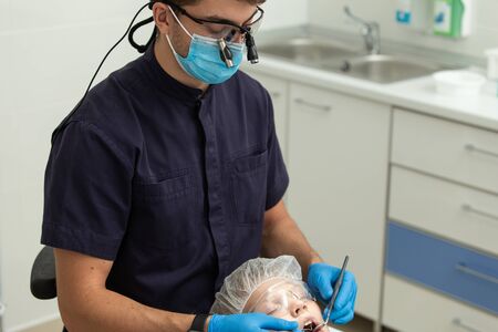 Confident dentist uses mirror and dental probe to check-up his patients gumsの写真素材