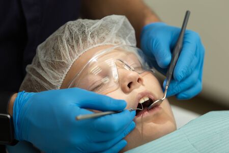 Little boy lays on dentist chair while doctor examines his teeths by probe and mirrorの写真素材