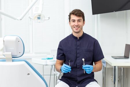 Handsome man wearing blue gloves holds dental probe and mirror in handsの写真素材