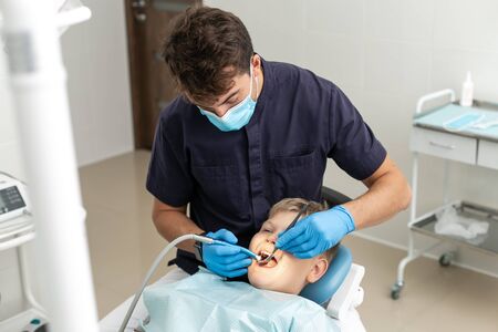 Dentist in black shirt drilling tooth of his young patientの写真素材
