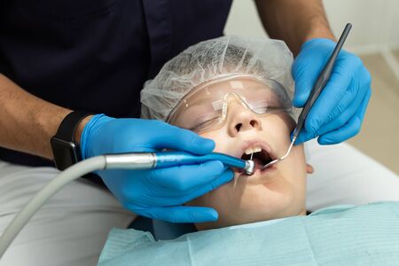 Stomatologist drilling teeths of patient who lies on dentist chairの写真素材