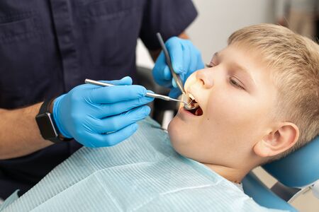 A young boy is lying on the dental chair and is being examinated by a doctorの写真素材
