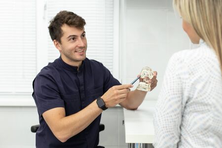 Smiling stomatologist holds pointing at model of jaw and talking with blond woman. Selective focusの写真素材