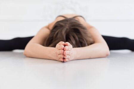 Blond woman in sport outfit doing splits on white bare floor. Selective focus.の写真素材